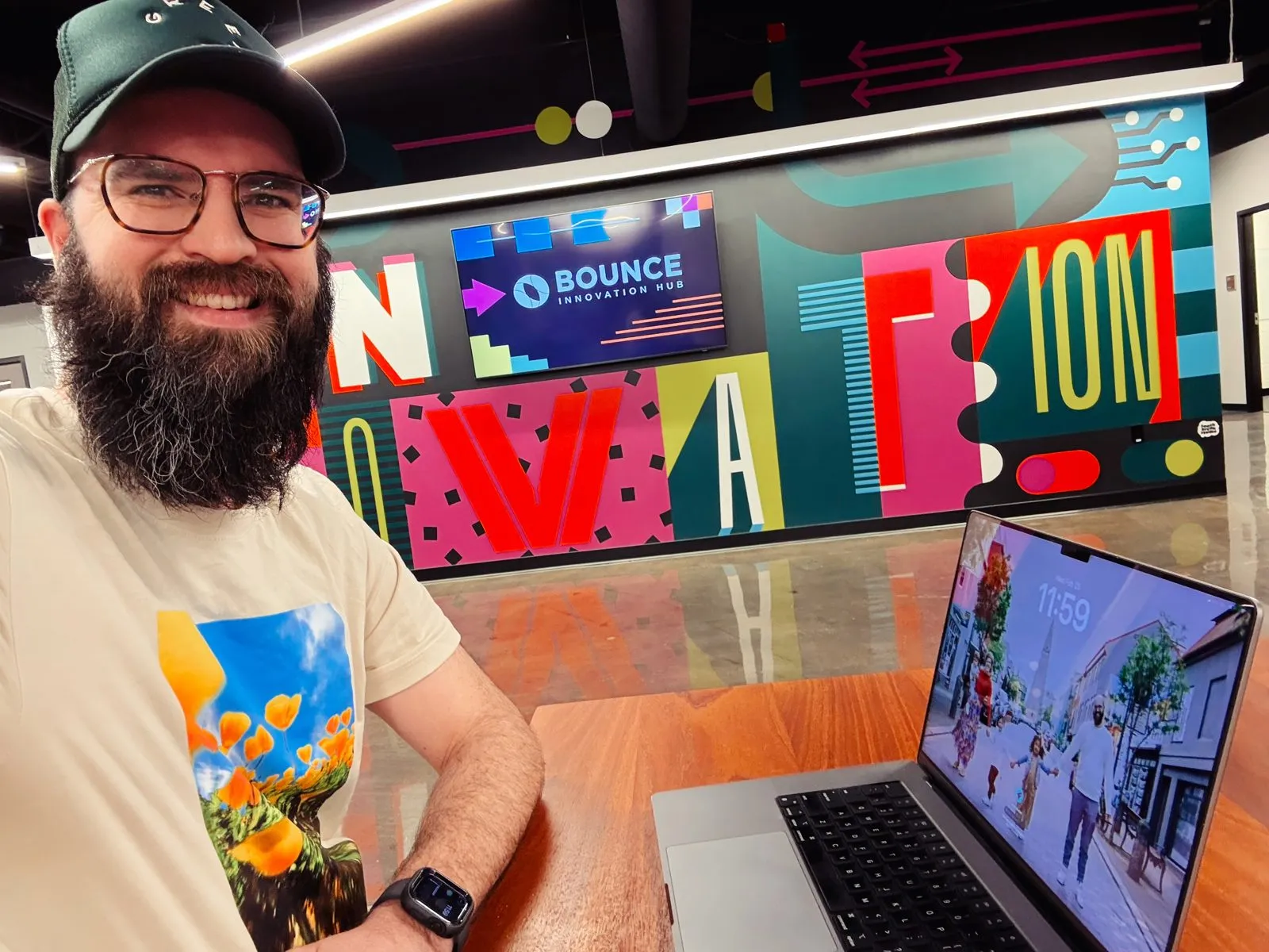 Jake grinning at his laptop in front of a colourful Bounce Innovation Hub mural