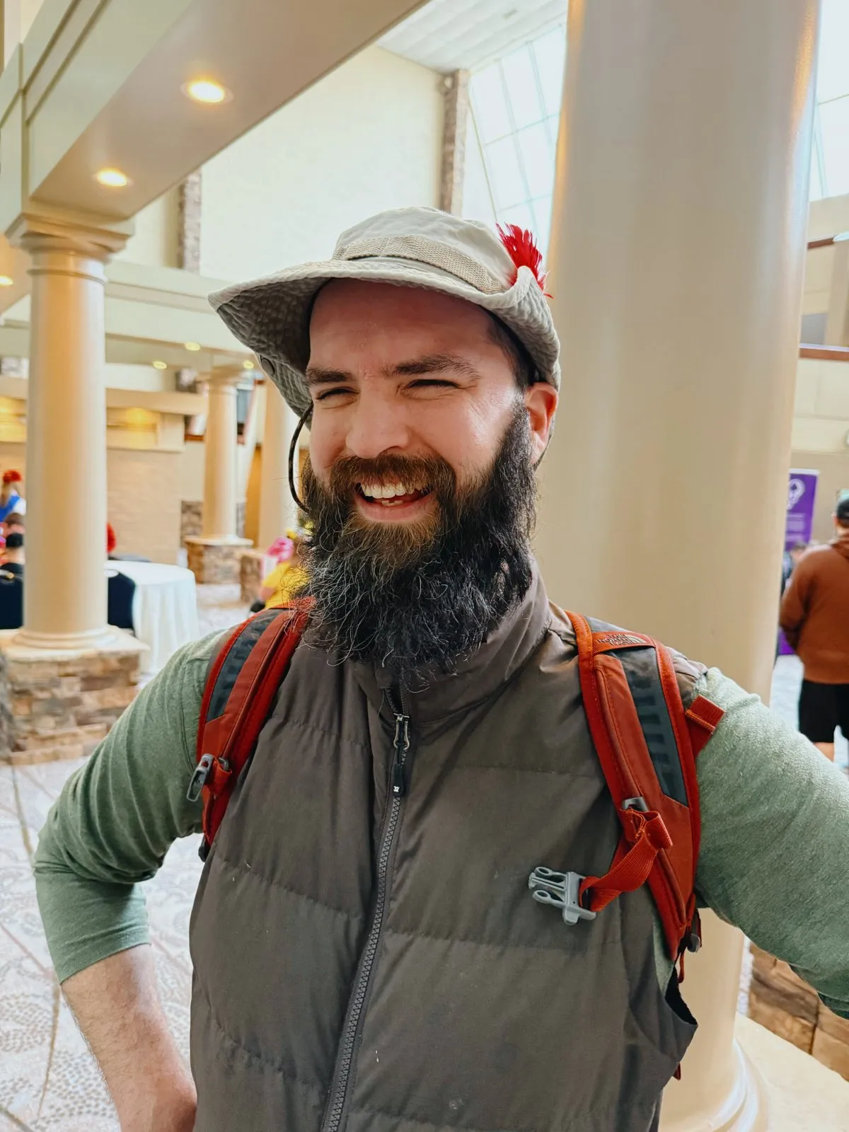 Jake grinning in a bucket hat and puffer vest, backpack straps on